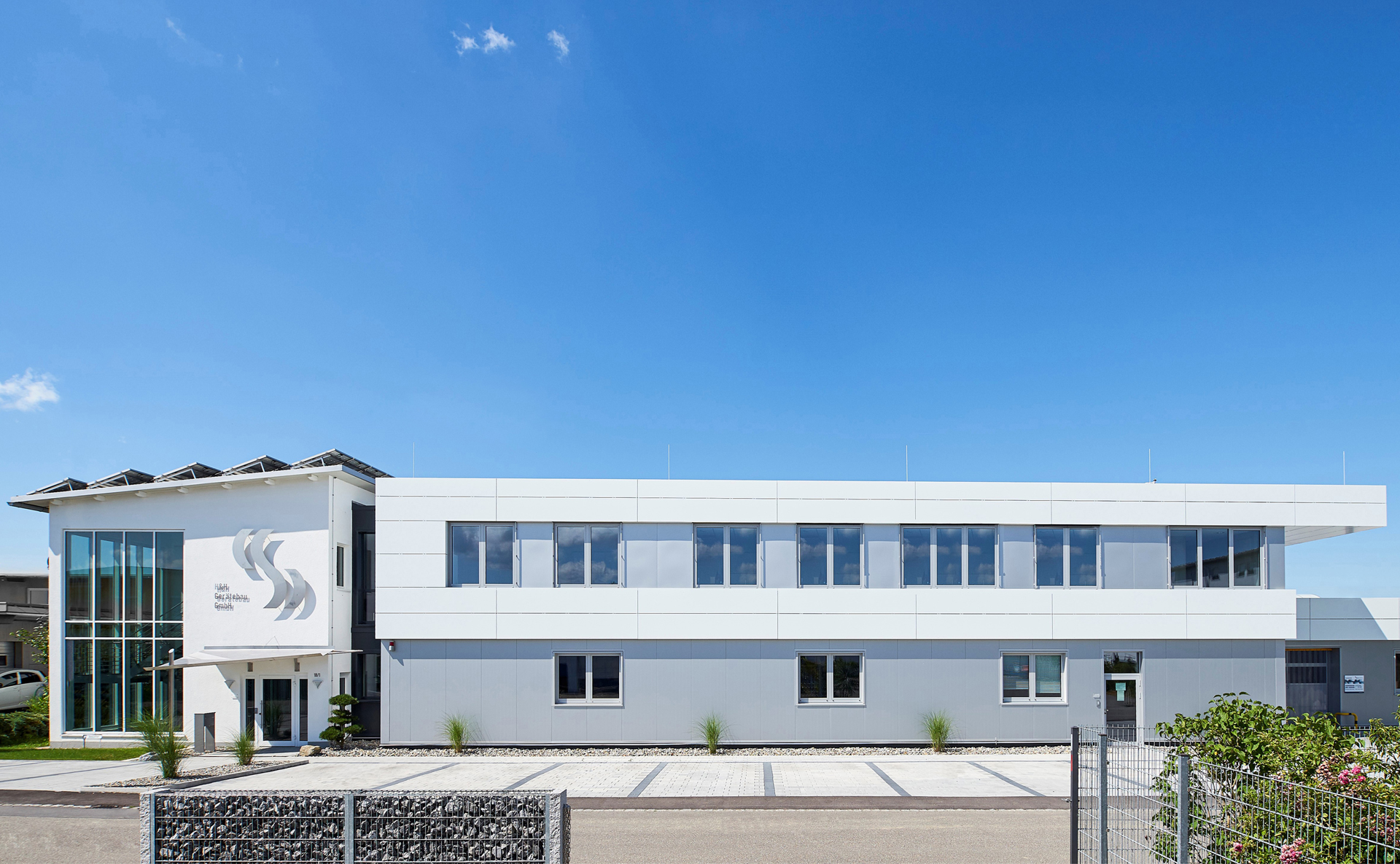 Das grau-weiße Firmengebäude von H&H Gerätebau unter blauem Himmel. 
